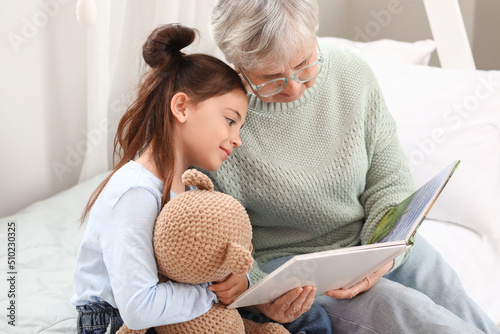 Canvastavla Little girl with toy and her grandma reading book in bedroom