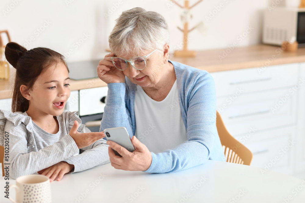Little girl with her grandma using mobile phone in kitchen Little girl with her grandma using mobile phone in kitchen