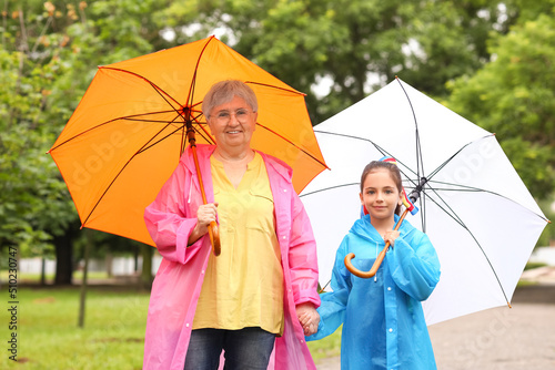 Little girl and her grandma in raincoats with umbrellas outdoors