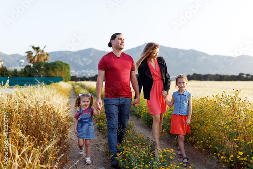 Happy family father of mother and two daughters sisters walking on countryside nature at sunset.Carefree parents having fun with their kids on a field.