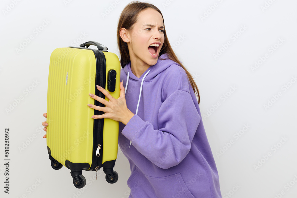 an emotional beautiful woman standing on a white background in a purple tracksuit clutched a suitcase with both hands holding it in front of her wrinkled her eyebrows and opened her mouth wide an emotional beautiful woman standing on a white background in a purple tracksuit clutched a suitcase with both hands holding it in front of her wrinkled her eyebrows and opened her mouth wide