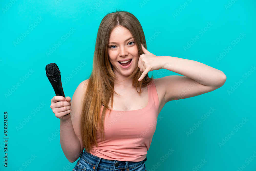 Singer caucasian woman picking up a microphone isolated on blue background making phone gesture. Call me back sign Singer caucasian woman picking up a microphone isolated on blue background making phone gesture. Call me back sign