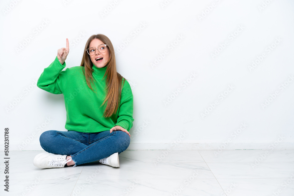 Young caucasian woman sitting on the floor isolated on white background intending to realizes the solution while lifting a finger up Young caucasian woman sitting on the floor isolated on white background intending to realizes the solution while lifting a finger up