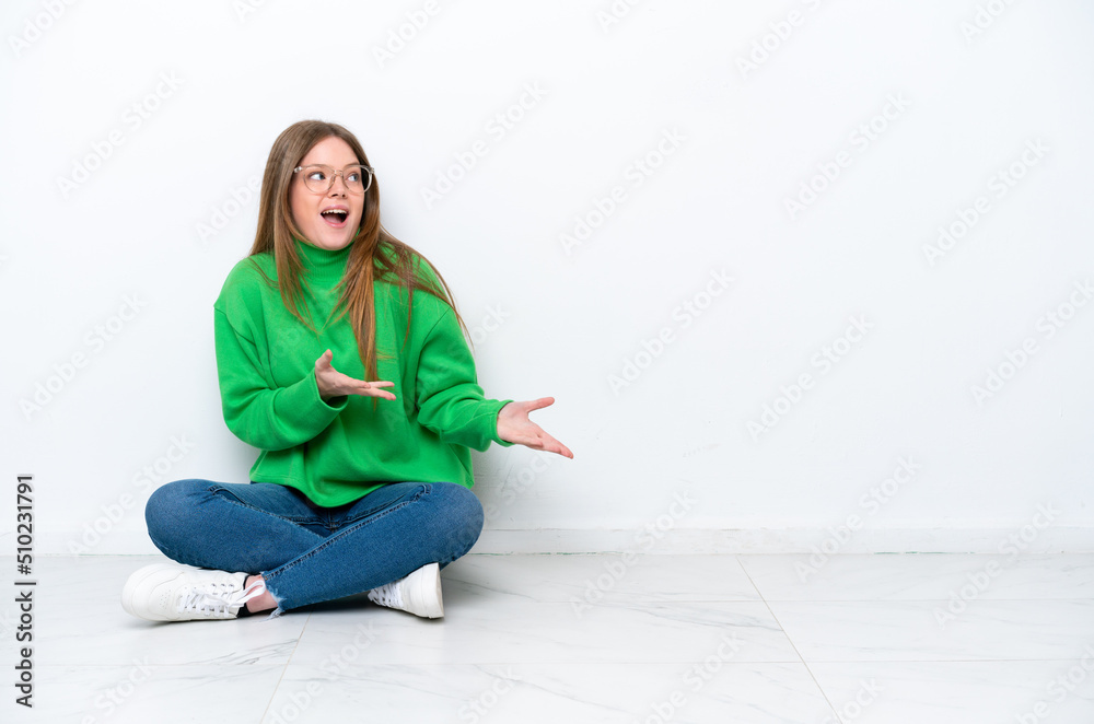Young caucasian woman sitting on the floor isolated on white background with surprise facial expression