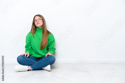 Young caucasian woman sitting on the floor isolated on white background and looking up