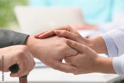 Doctor touching hand of patient with cane in clinic, closeup