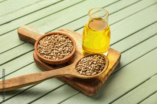 Bottle of oil, bowl, spoon with sunflower seeds and board on green wooden background
