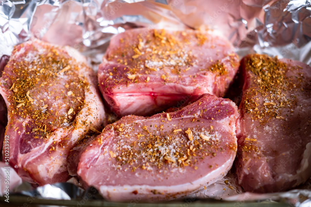 Raw meat steaks on foil. Pork meat sprinkled with spices. Cooking without oil. Preparation for cooking in the oven.