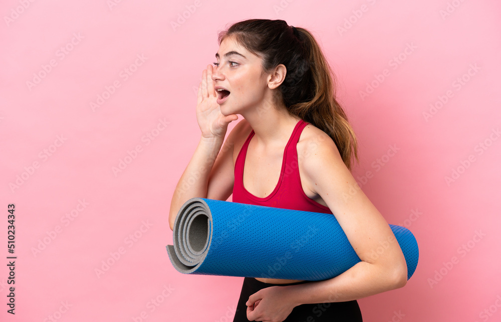 Young sport woman going to yoga classes while holding a mat shouting with mouth wide open to the side Young sport woman going to yoga classes while holding a mat shouting with mouth wide open to the side