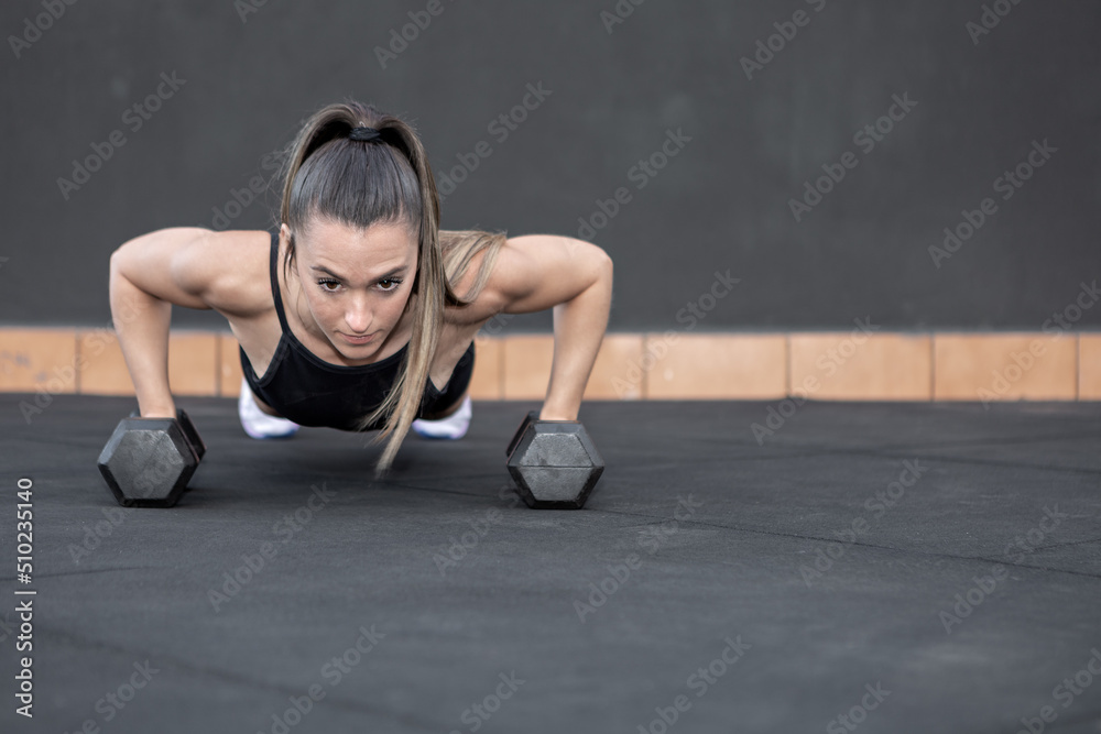 Sportswoman doing push ups on dumbbells