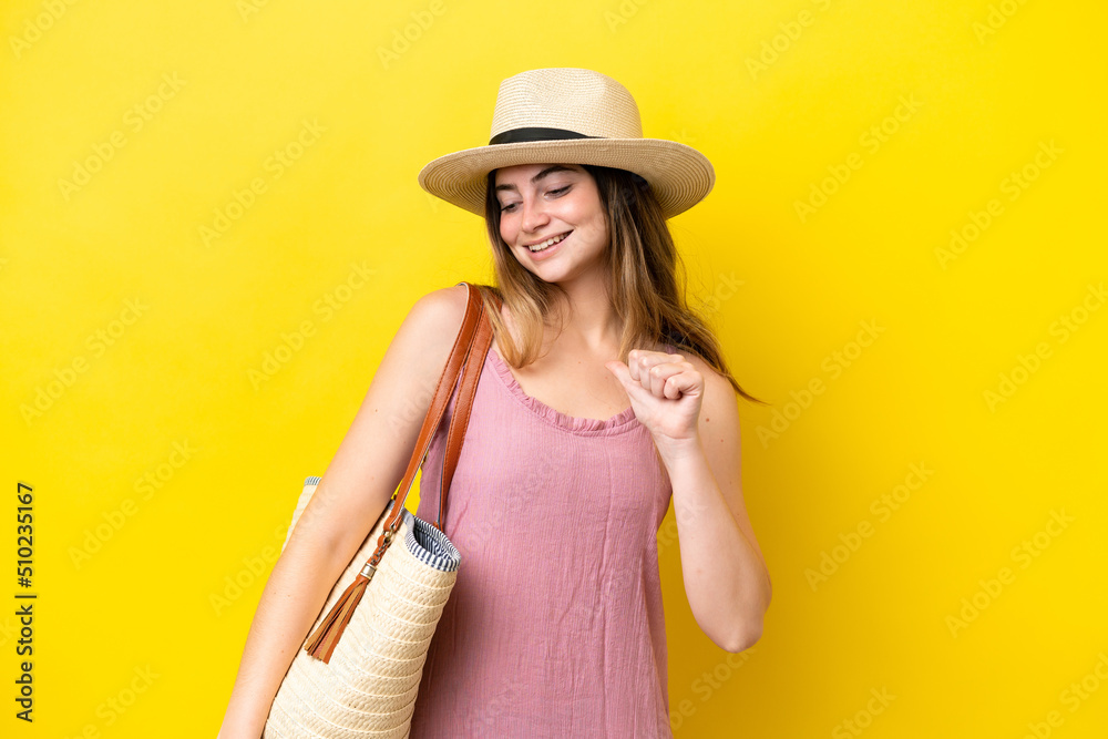Young caucasian woman holding a beach bag isolated on yellow background proud and self-satisfied