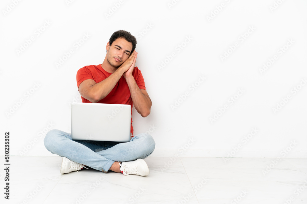 Caucasian handsome man with a laptop sitting on the floor making sleep gesture in dorable expression Caucasian handsome man with a laptop sitting on the floor making sleep gesture in dorable expression