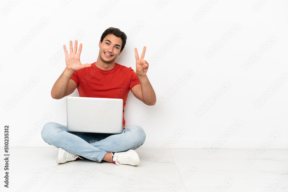 Caucasian handsome man with a laptop sitting on the floor counting seven with fingers Caucasian handsome man with a laptop sitting on the floor counting seven with fingers
