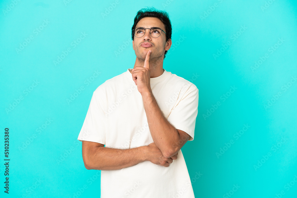 Caucasian handsome man over isolated blue background having doubts while looking up Caucasian handsome man over isolated blue background having doubts while looking up