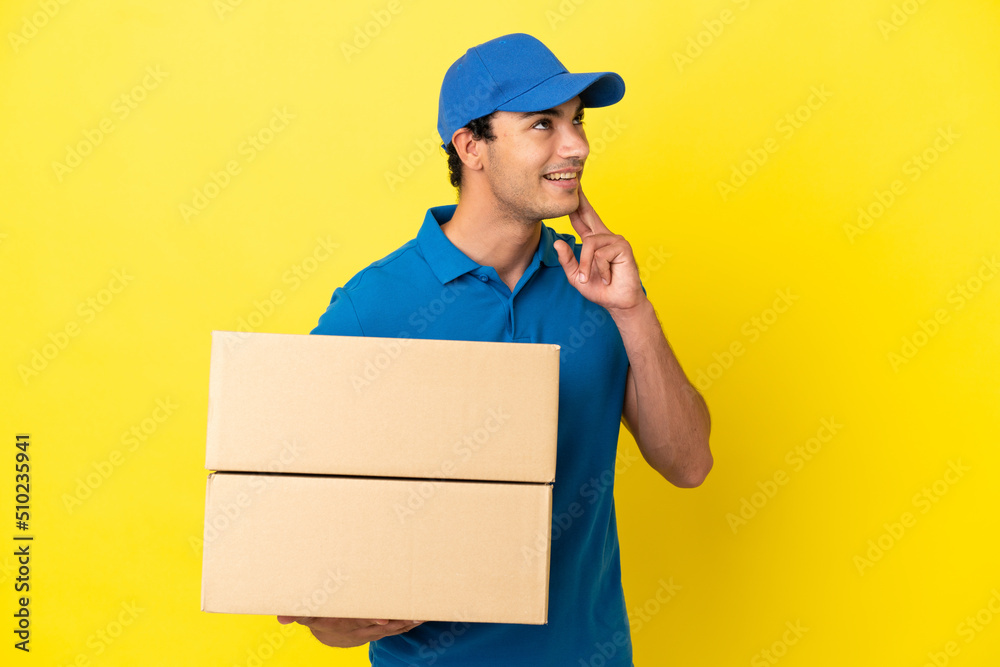 Delivery man over isolated yellow wall thinking an idea while looking up Delivery man over isolated yellow wall thinking an idea while looking up