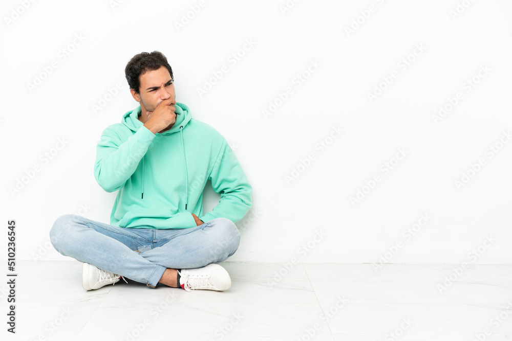 Caucasian handsome man sitting on the floor having doubts and with confuse face expression Caucasian handsome man sitting on the floor having doubts and with confuse face expression