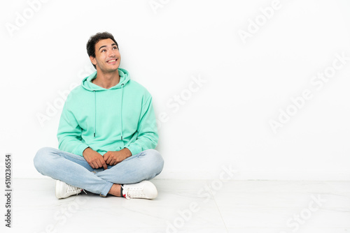 Caucasian handsome man sitting on the floor looking up while smiling