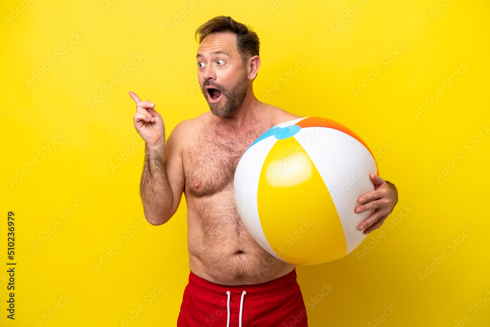 Middle age caucasian man holding beach ball isolated on yellow background intending to realizes the solution while lifting a finger up