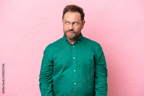 Middle age caucasian man isolated on pink background having doubts while looking up © luismolinero
