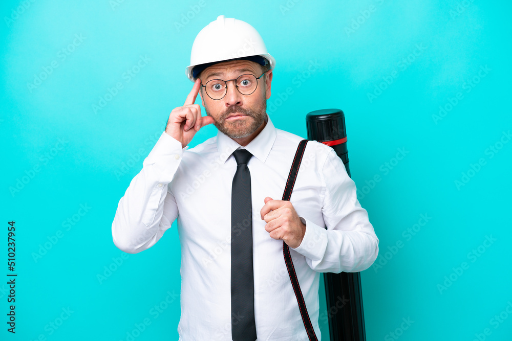 Middle age architect man with helmet and holding blueprints isolated on blue background thinking an idea Middle age architect man with helmet and holding blueprints isolated on blue background thinking an idea