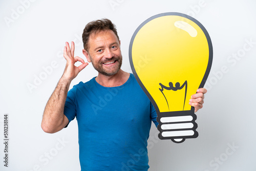 Middle age caucasian man isolated on white background holding a bulb icon and doing OK sign