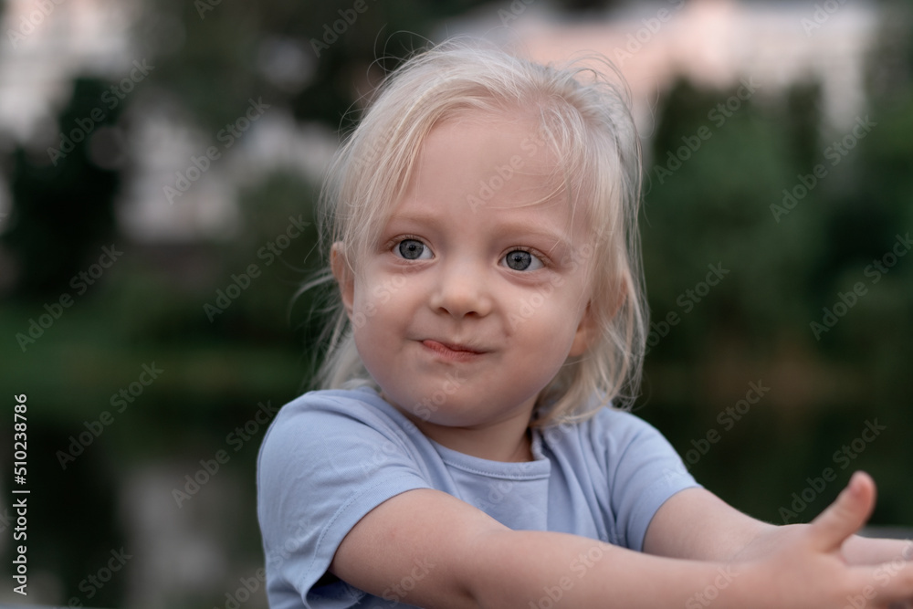 Portrait of little blonde girl with big eyes wears blue T-shirt and looks into the distance. Childlike spontaneity. Portrait of little blonde girl with big eyes wears blue T-shirt and looks into the distance. Childlike spontaneity.