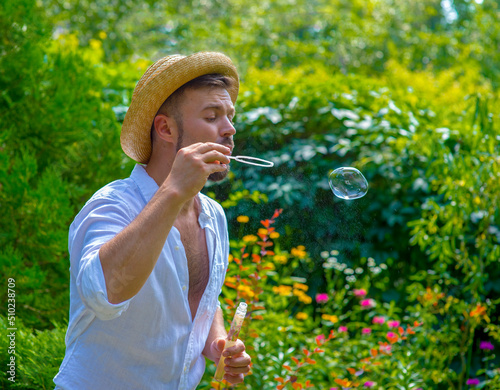 the guy blows soap bubbles in the garden against the background of green plants