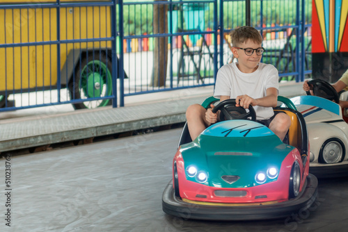 Portrait of teenage boy in glasses driving an electric car in amusement park. Child on Bumper car. photo