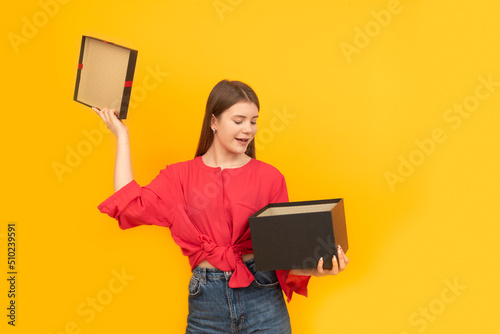 Woman with large black box. Surprised happy young girl holds an open gift. Bright yellow background