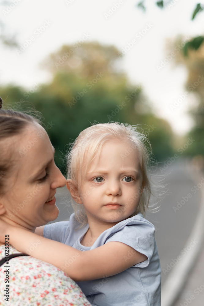 Young mother holds serious daughter in her arms and smiling sweetly. Portrait of mother and blonde girl. Young mother holds serious daughter in her arms and smiling sweetly. Portrait of mother and blonde girl.