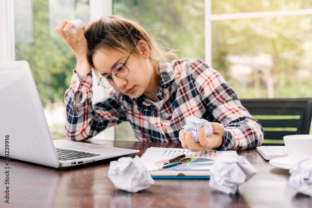 Woman stressed about work at home office and look at something on the laptop screen and holding lump of paper in hand, The stress gave her a huge headache. Woman stressed about work at home office and look at something on the laptop screen and holding lump of paper in hand, The stress gave her a huge headache.