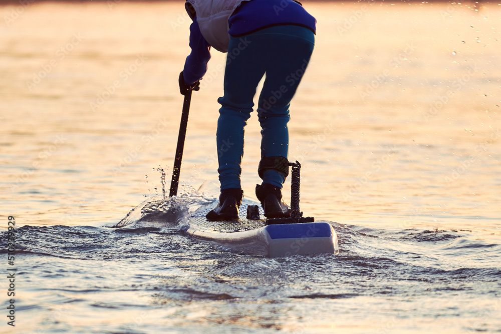 Legs of a man on stand up paddle board (SUP) with a paddle at winter river at dawn Legs of a man on stand up paddle board (SUP) with a paddle at winter river at dawn