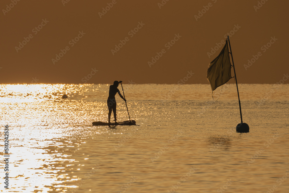 Silhouette of a girl floating on a sup board against the background of sunrise