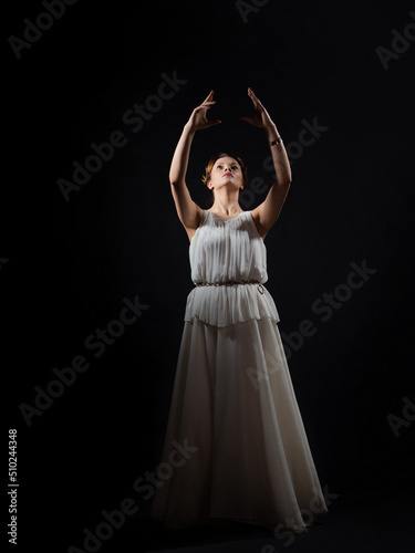 An ancient heroine asks the gods, a young woman in the ancient Greek style stretches her hands to the sky. A noble heroine in a white tunic and a laurel wreath,