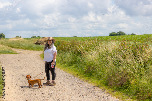 Tableau sur toile Mature woman walking with her short-haired brown dachshund, hiking trail between