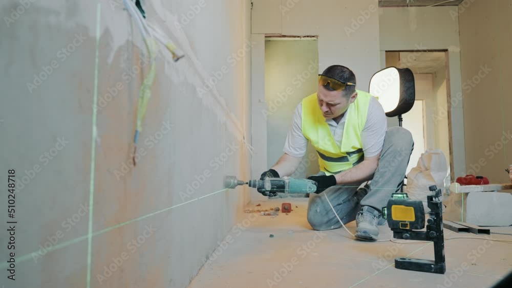 View on top Construction worker drills a hole in the wall under the socket. The level of the hole for the electrical outlet is set by a laser.