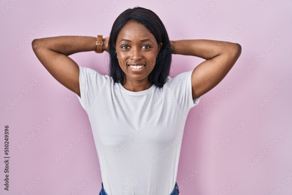 African young woman wearing casual white t shirt relaxing and stretching, arms and hands behind head and neck smiling happy