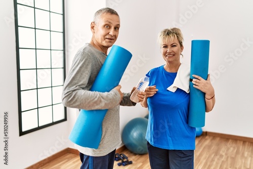 Senior caucasian sporty couple smiling happy holding yoga mat and bottle of water at sport center.