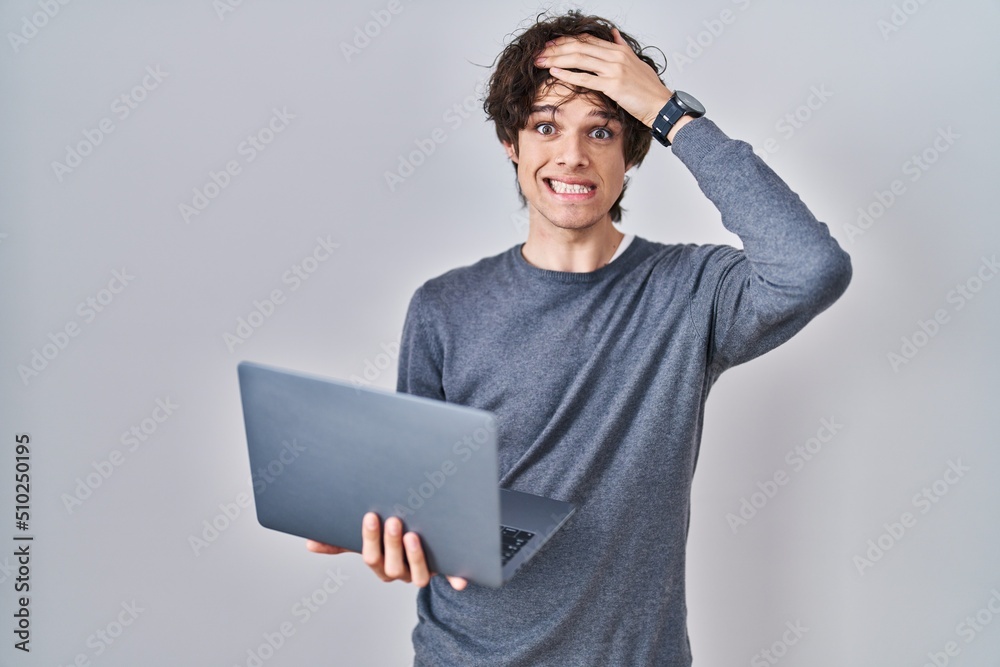 Young man working using computer laptop stressed and frustrated with hand on head, surprised and angry face Young man working using computer laptop stressed and frustrated with hand on head, surprised and angry face