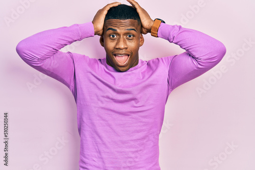 Young black man wearing casual pink sweater crazy and scared with hands on head, afraid and surprised of shock with open mouth
