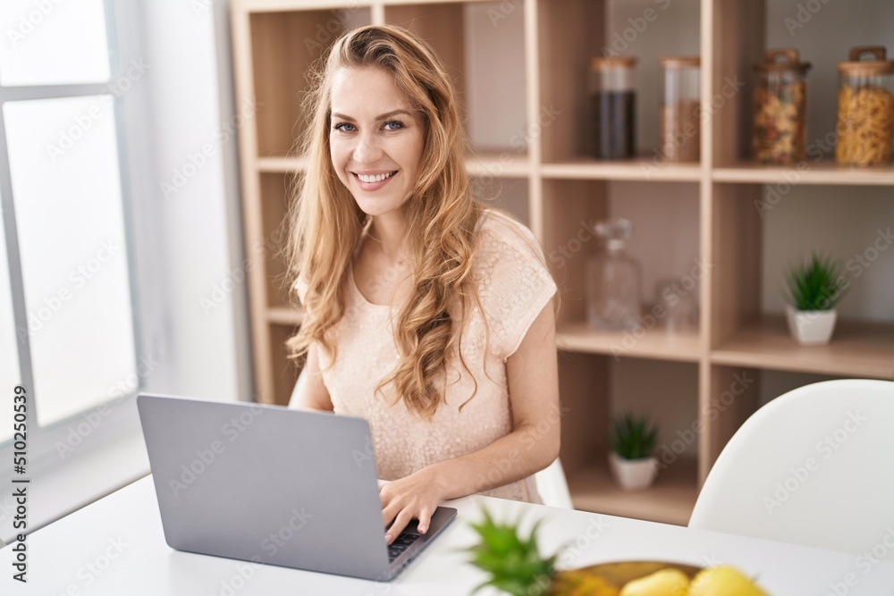Young blonde woman using laptop sitting on table at home Young blonde woman using laptop sitting on table at home