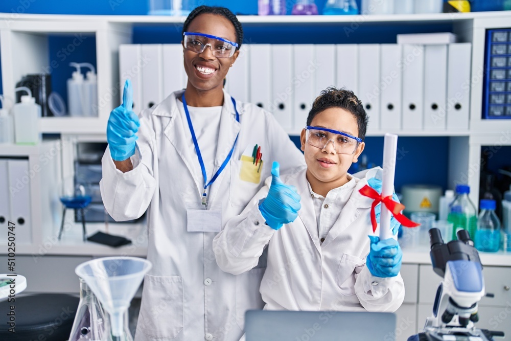 Mother and son at scientist laboratory smiling happy and positive, thumb up doing excellent and approval sign Mother and son at scientist laboratory smiling happy and positive, thumb up doing excellent and approval sign