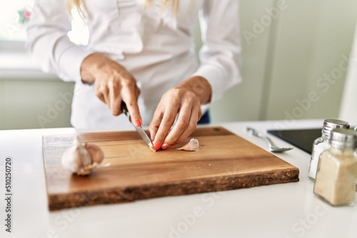 Young blonde woman cutting garlic at kitchen