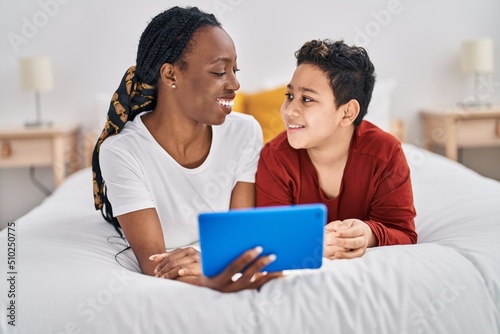 African american mother and son using touchpad lying on bed at bedroom