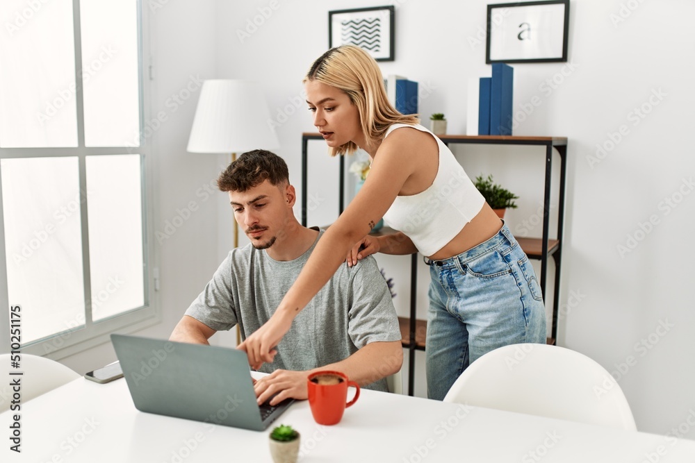 Obraz premium Young caucasian couple using laptop and drinking coffee sitting on the table at home.