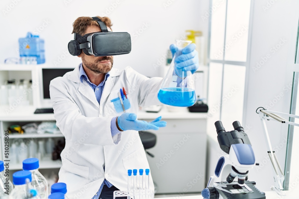 Middle age hispanic man wearing scientist uniform using vr glasses holding test tube at laboratory Middle age hispanic man wearing scientist uniform using vr glasses holding test tube at laboratory