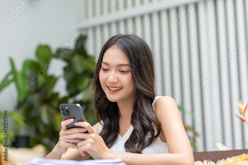 Happy asian young woman smile using smartphone surfing internet and enjoy with social media or online shopping at home. Modern wellness life of cute female looking at mobile phone fun and happiness