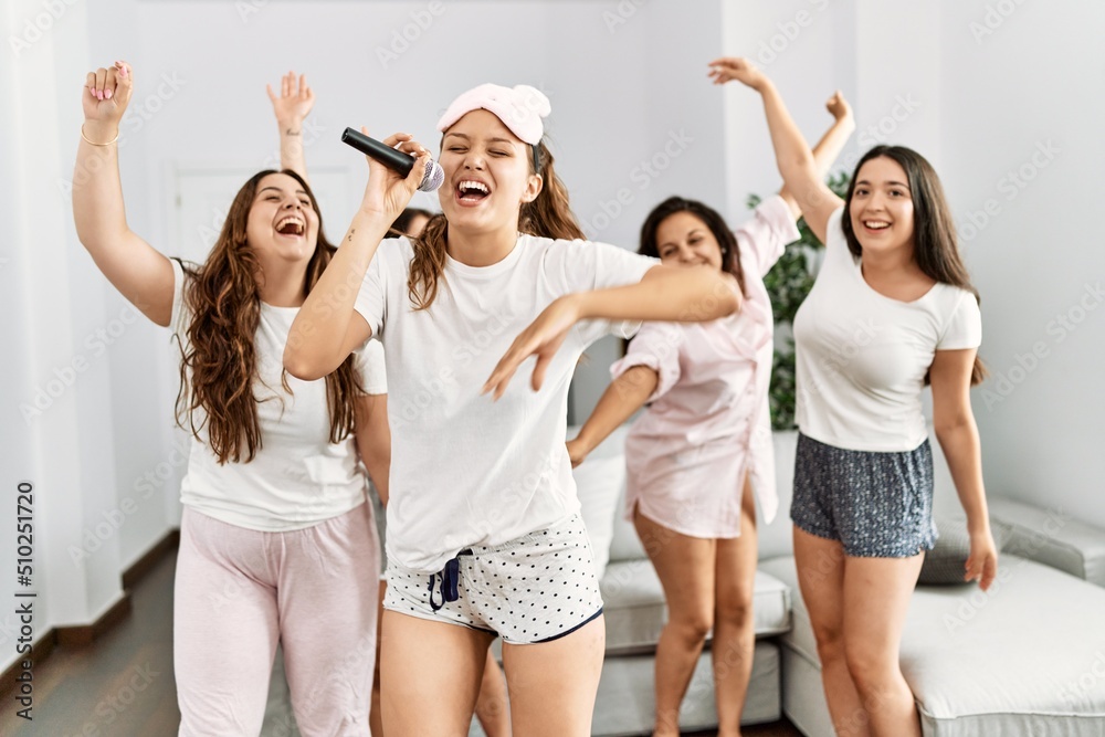 Naklejka premium Group of young hispanic women celebrating pajamas party singing song and dancing at home.