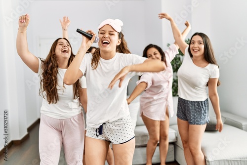 Group of young hispanic women celebrating pajamas party singing song and dancing at home.