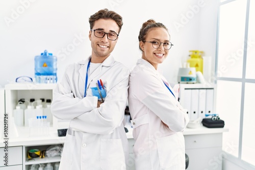 Man and woman wearing scientist uniform standing with arms crossed gesture at laboratory
